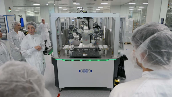 Man sieht Personen in sterilen Anzügen, die einen Roboter mit mehreren Armen beobachten.