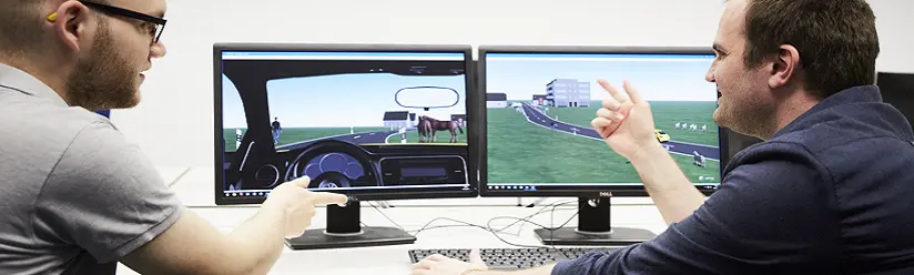 Quelle: THI Zwei wissenschaftliche Mitarbeiter besprechen eine Fahrsimulation am Bildschirm