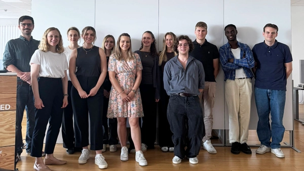 Ein Gruppenfoto von 12 Personen vor einer weißen Wand. 