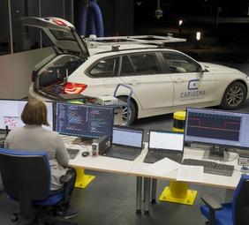 Source: THI Image of a woman sitting in front of two screens. On which system tests of applications based on Car2X communication are running