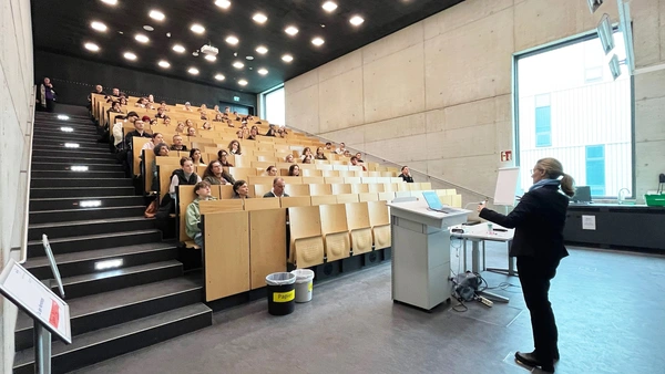 A woman gives a lecture in front of a full lecture theatre. 