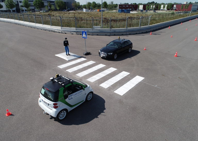 Quelle: THI Abbildung von zwei autonom fahrender Fahrzeugen, die jeweils auf einer Seite eines Zebrastreifens stehen, den ein Dummy-Fußgänger überqueren möchte.