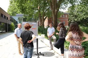 Forscherinnen und Forscher aus unterschiedlichen Disziplinen diskutierten Lösungen (Foto: THI). Fünf Personen im Außenbereich des Campus in Neuburg, die vor einer Pinnwand mit unterschiedlichen Tags stehen und dieskutieren